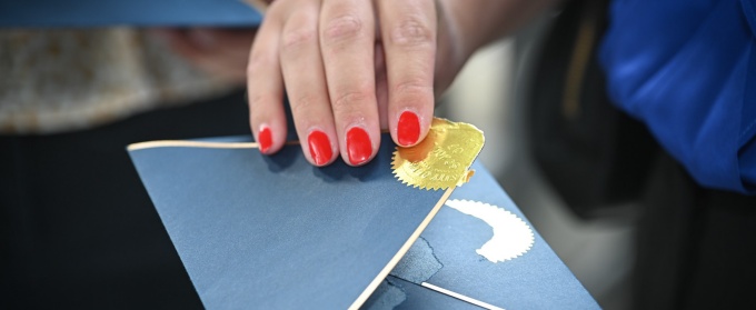 Blue envelope with a gold seal being opened. 