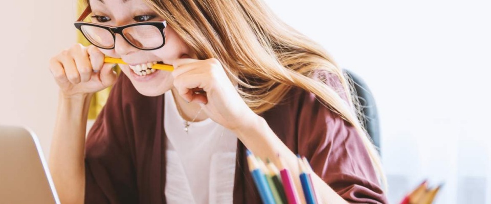 woman looking at a laptop nervously biting on a pencil. 