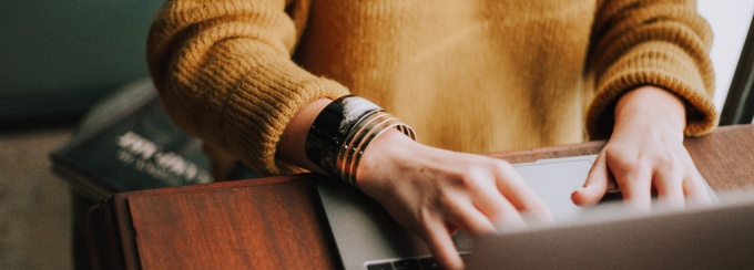 photo of person in yellow sweater typing on a Mac laptop, only their arm and hand is showing. 