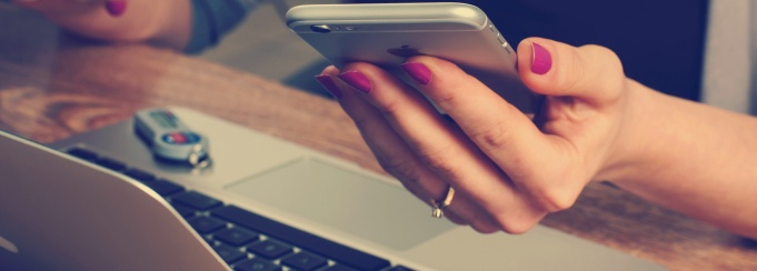 Photo of a girl in a coffee shop on her laptop with a phone in one hand. 