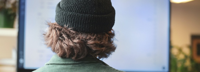 the back of a man's head with a hat on facing a computer screen. 