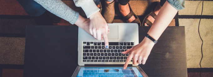 three people pointing at a laptop screen from a birdseye view. 