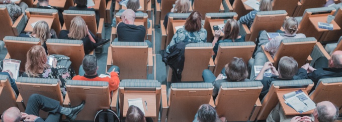 photo of a lecture hall filled with people facing away from the camera. 