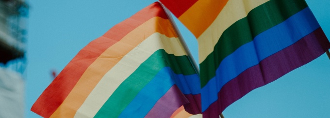 close up image of two Pride flags waving with blue sky in the background. 