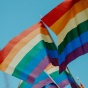 close up image of two Pride flags waving with blue sky in the background. 