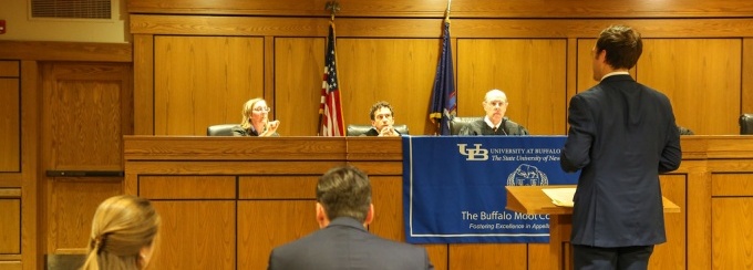 Picture of a student attorney at a podium in a courtroom speaking to a panel of judges. 