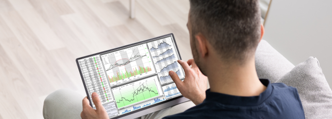 A man sitting on the couch looking at a tablet displaying stocks. 