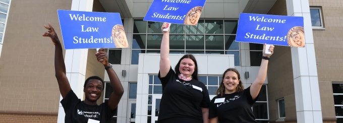 Photo three students are holding signs that say Welcome Law Students. 