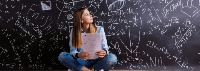 Women sitting on the floor in front of a chalkboard full of math problems. 