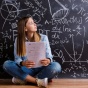 Women sitting on the floor in front of a chalkboard full of math problems. 