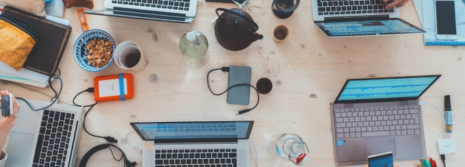 photo of laptops on a desk and hands pointing at the laptop screens. 