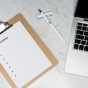 A clipboard with application, pen, and laptop on a marble table. 