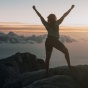 women standing proudly atop a mountain, above the clouds, during sunrise. 