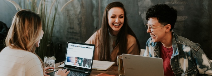 Photo of three people laughing and working on laptops in a dark cafe. 