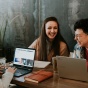 Photo of three people laughing and working on laptops in a dark cafe. 