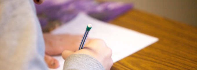 woman holding a pencil writing on a paper on a desk. 