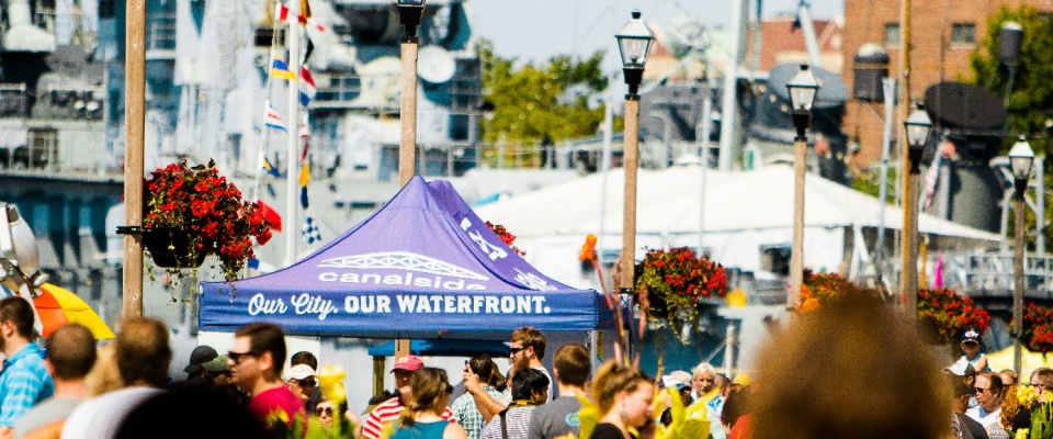 A crowd of people in front of Buffalo's Canalside side with Our City Our Waterfront pop-up tent. 