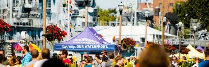 A crowd of people in front of Buffalo's Canalside side with Our City Our Waterfront pop-up tent. 