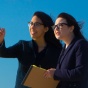 Two students are in front of windmills on Lake Erie having a discussion. 