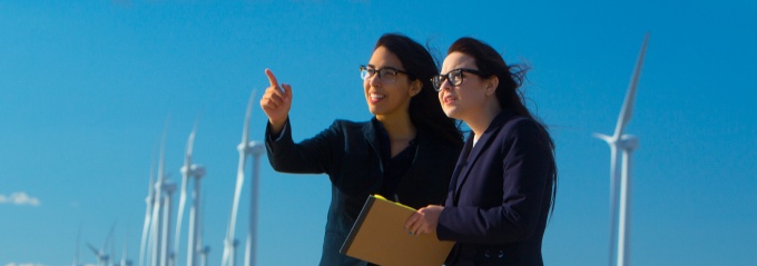 Two students are in front of windmills on Lake Erie having a discussion. 