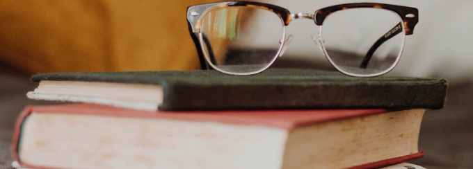 Photo of books on a desk with glasses set on top. 