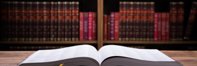 An open book on a table in front of a bookshelf with law books. 