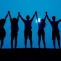 shadow of a group of people holding hands up in front of blue sky. 