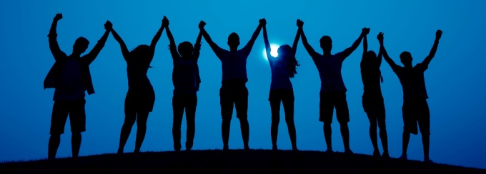 shadow of a group of people holding hands up in front of blue sky. 