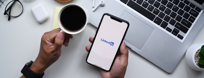 A person holding a phone with LinkedIn on it and a cup of coffee. 