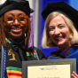 Award recipient and faculty member in academic regalia display a framed certificate during a law school commencement ceremony. 