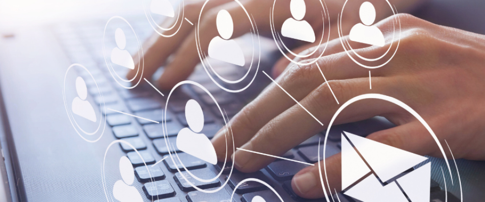 Hands typing on a laptop keyboard with digital icons overlaid, including multiple user profile symbols connected by lines and a large envelope icon, representing email communication and networking. 