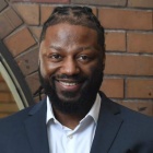 man standing next to a brick wall, smiling. 