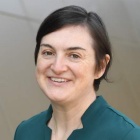 woman wearing green shirt, standing outside, smiling. 