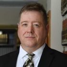 man standing in a room with bookshelves, wearing tie, smiling. 