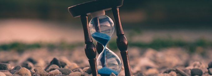 photo of an hourglass with blue sand in a field. 