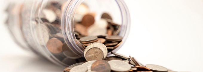 a jar with coins spilled over on a white countertop. 