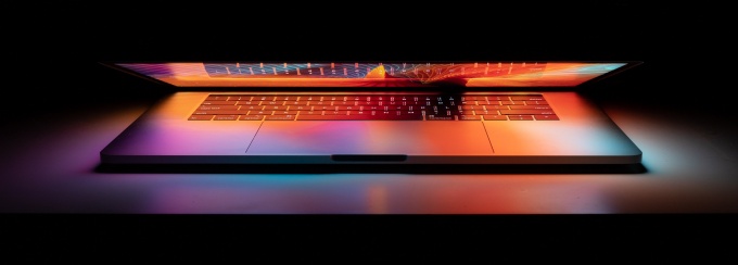 a laptop slightly open with the light glowing in a dark room. 