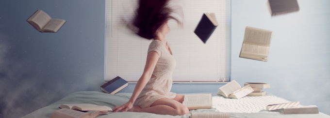 photo of a person sitting on a bed with books flying in the air. 