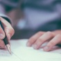 photo of man with pen in his hand, writing on a piece of paper. 