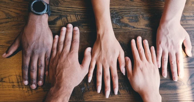 table top with 5 hands of varying skin color. 