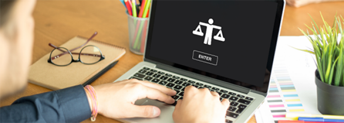 A person uses a laptop displaying the word “ETHICS” with an icon of a figure holding scales and a button labeled “ENTER.” The desk includes notebooks, colored pencils in a holder, and a potted plant, suggesting a workspace focused on ethical learning or research. 