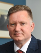 man wearing suit and tie, sitting in a room with a painting on a blue wall. 