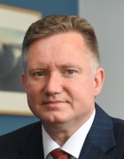 S. Todd Brown wearing suit and tie, sitting in a room with a painting on a blue wall. 