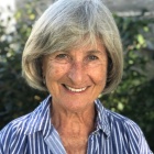 Smiling woman wearing blue and white striped shirt, standing outside near some green bushes. 