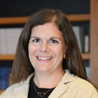 A professional portrait of Katrin Rowan standing in a room with several legal books on shelves. 