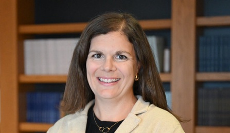 A professional portrait of Katrin Rowan standing in a room with several legal books on shelves. 