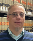 man wearing glasses standing in front of a bookcase with legal books. 