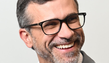 Portrait of Prof. Chiesa wearing glasses, a light blue blazer. 