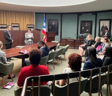 people inside a government room, listening to a speaker. 