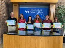 group of people standing in front of a sign that says University at Buffalo School of Law, each person holding up signs. 